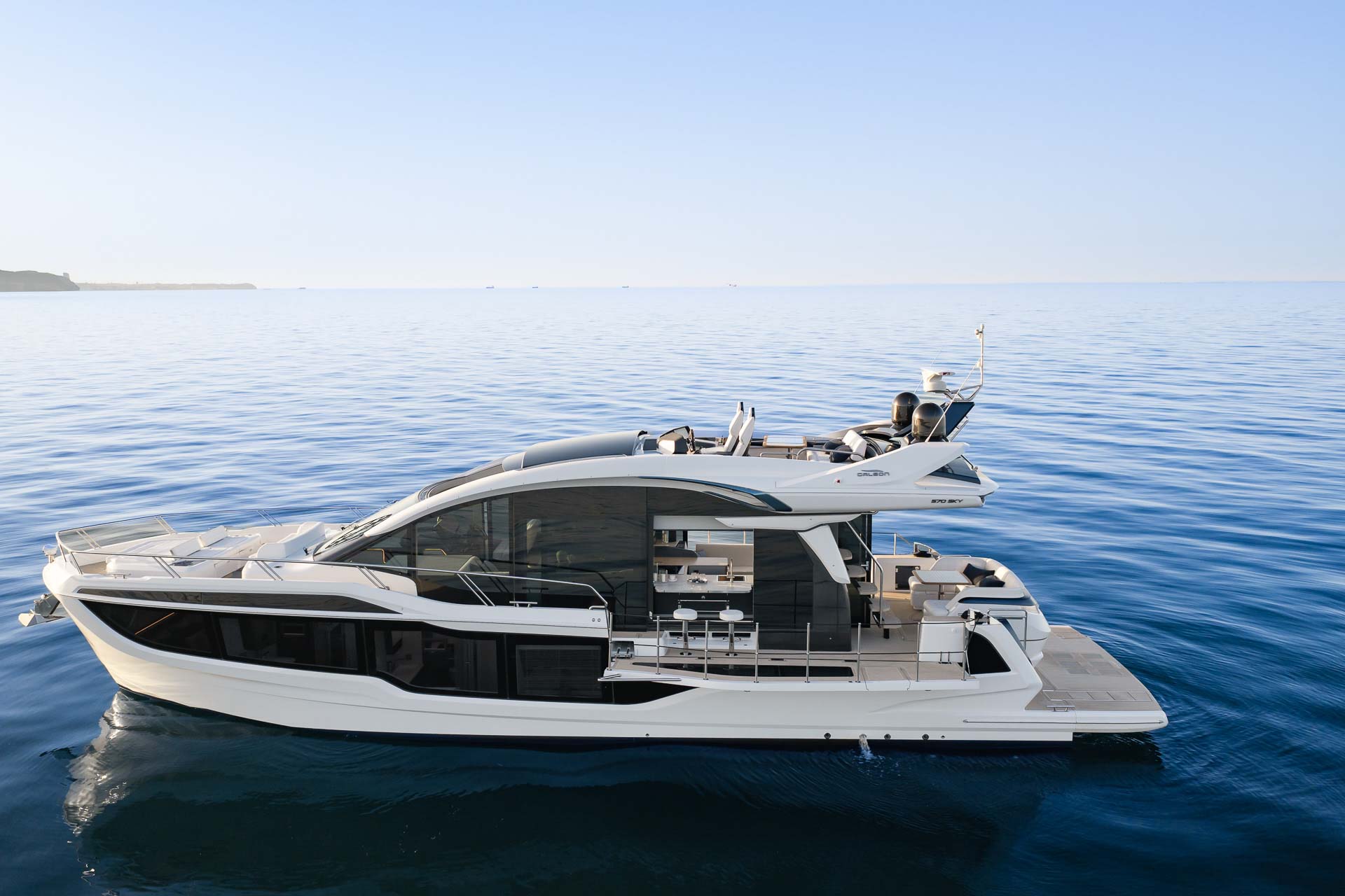 Galeon 570 SKY seen in profile on flat blue water, Beach Mode balconies folded out.
