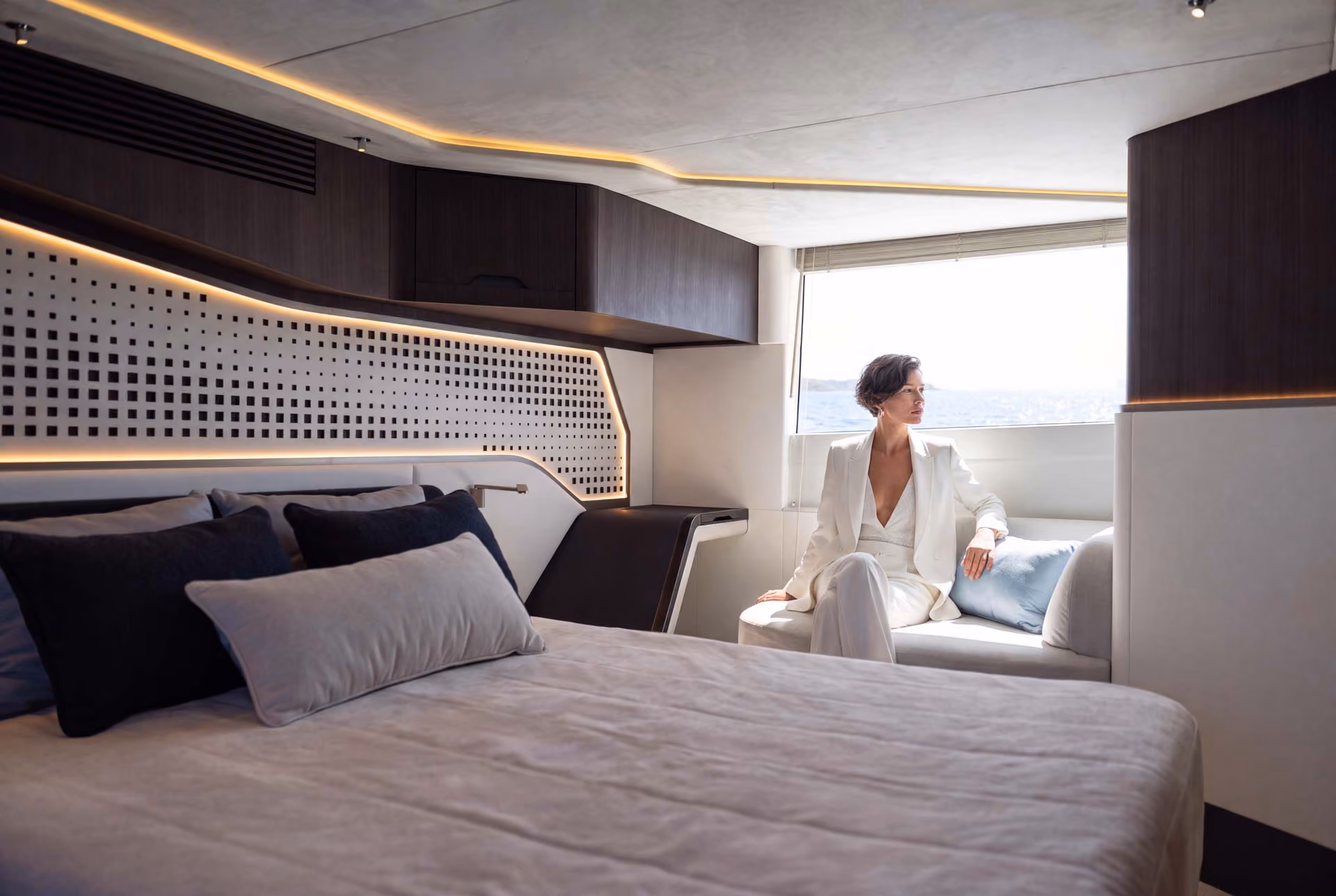 Woman seated by the window in the Galeon 570 SKY master cabin, wooden headboard behind.