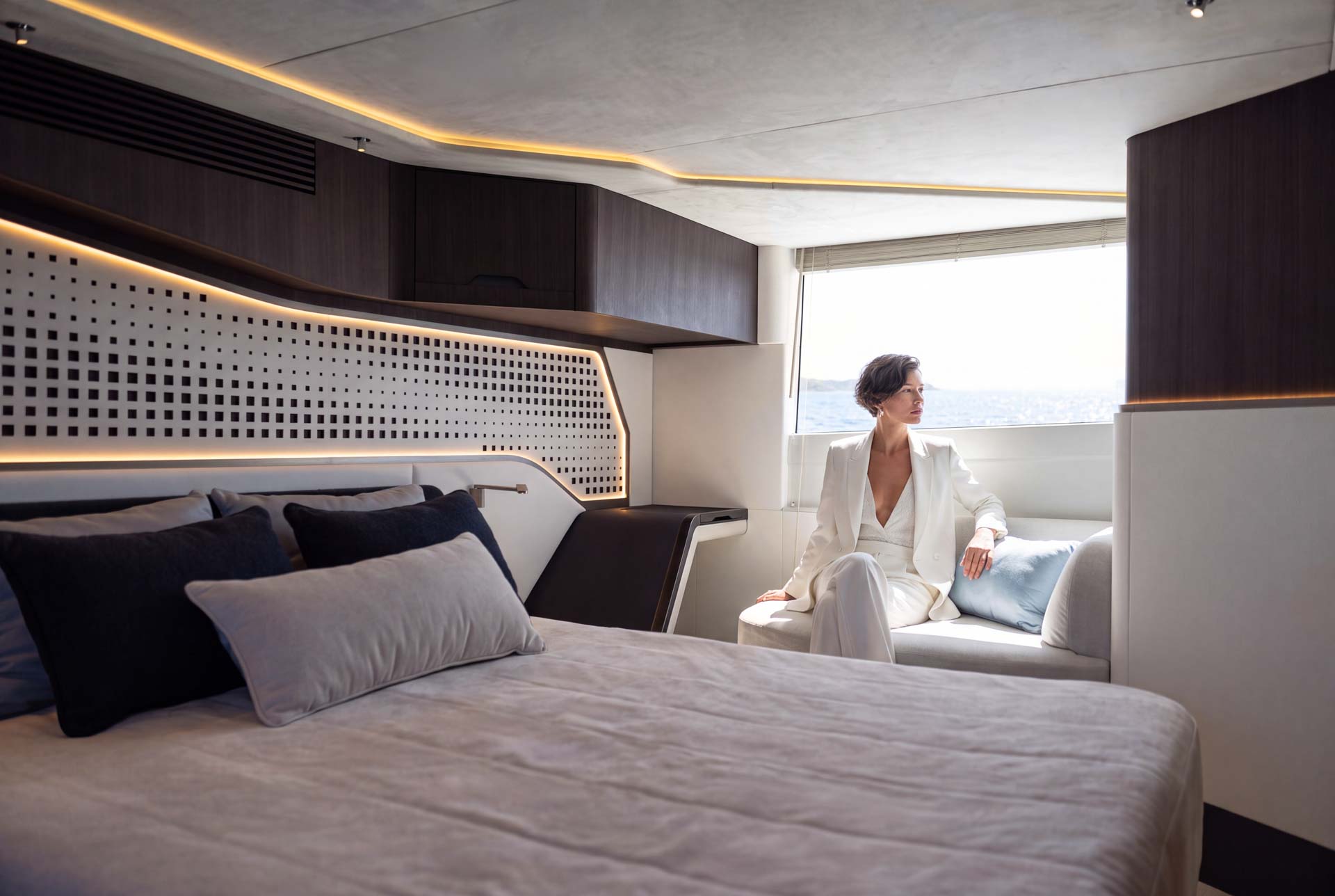 Woman seated by the window in the Galeon 570 SKY master cabin, wooden headboard behind.
