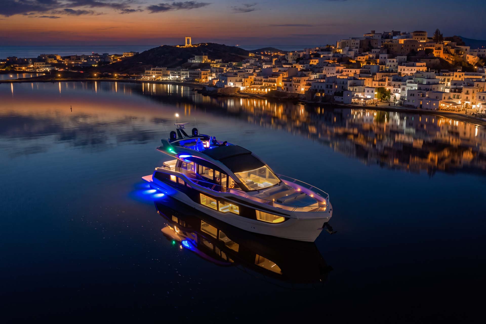 Aerial view of the Galeon 570 SKY lit at night in a calm bay.