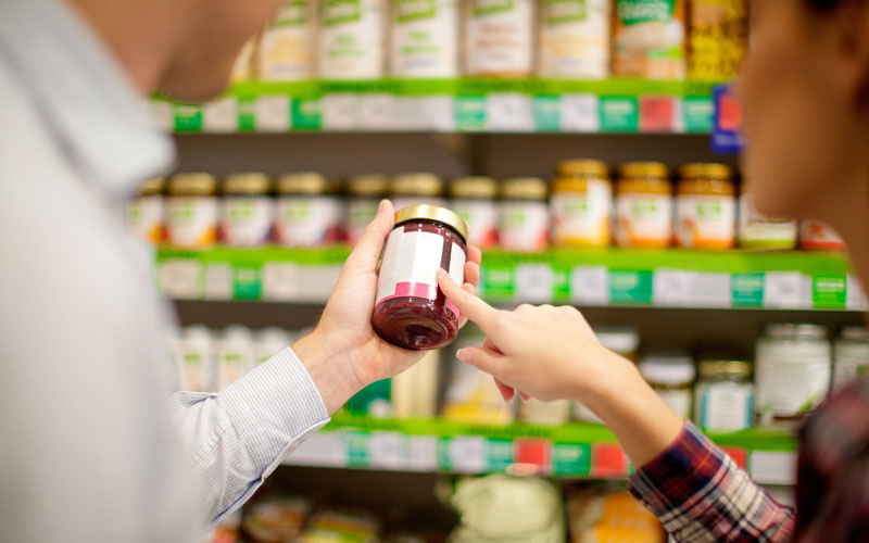 A man and a woman inspect the nutrition label of a jarred food.