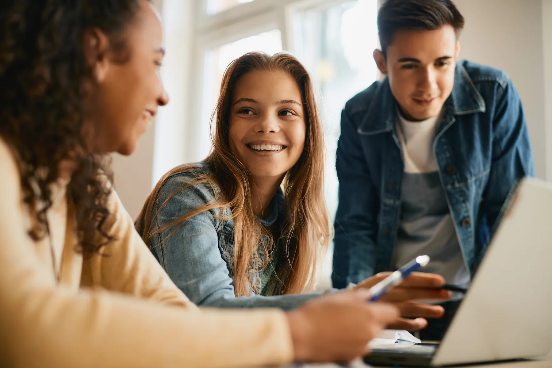 A smiling student working at a laptop with two classmates.
