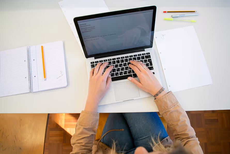 a person typing on a computer next to papers