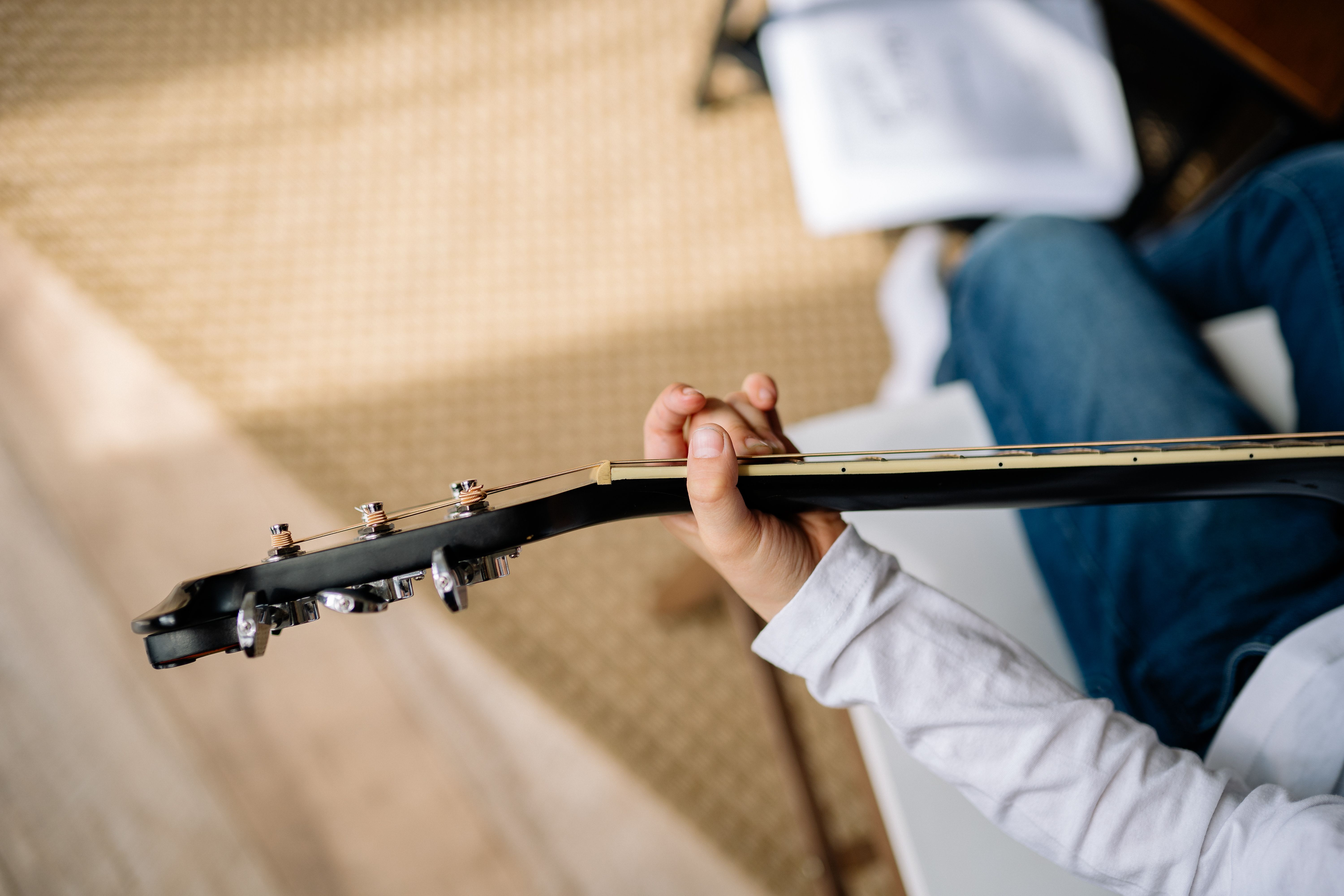 A student plays an acoustic guitar while seated at home, representing meaningful engagement in an extracurricular pursued out of genuine interest.