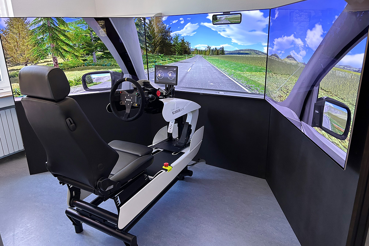 Fahrsimulator mit Stuhl, Lenkrad und drei Bildschirmwänden zeigt Landstraße für Fahrtraining.