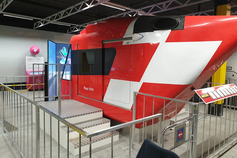 Roter Hubschraubersimulator mit weißem Kreuz und Treppe, abgesperrt mit Metallgeländer.
