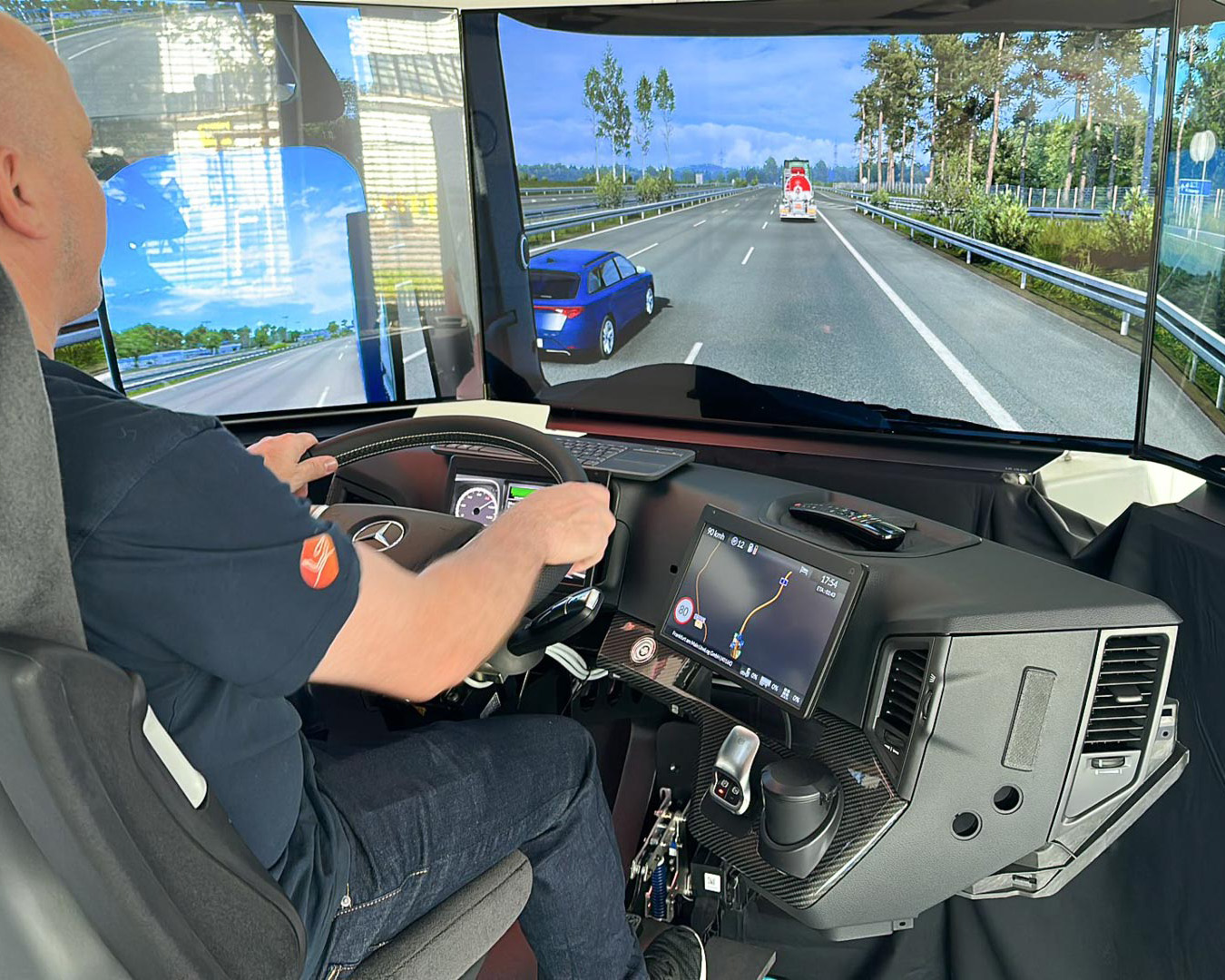 Fahrzeugfahrer sitzt an Lenkrad vor drei Bildschirmen mit digitaler Straßenansicht und Navigationskarte.