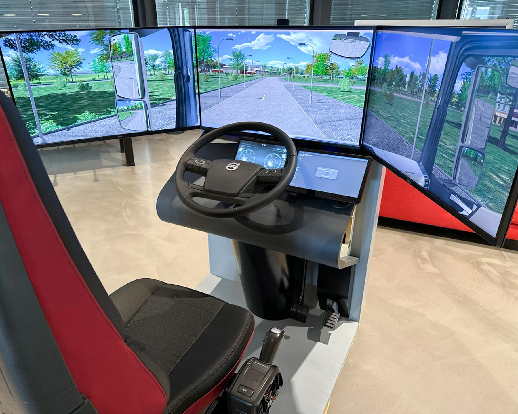 Lastfahrersimulator mit Lenkrad, Schalthebel, Pedalen und drei Monitoren mit Straßenansicht.