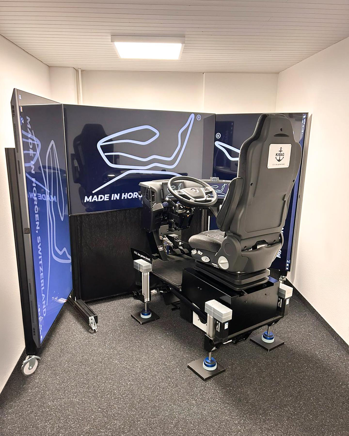 LKW-Fahrsimulator mit Lenkrad, Pedalen und Displays, beschriftet mit „Made in Horgen, Schweiz“.