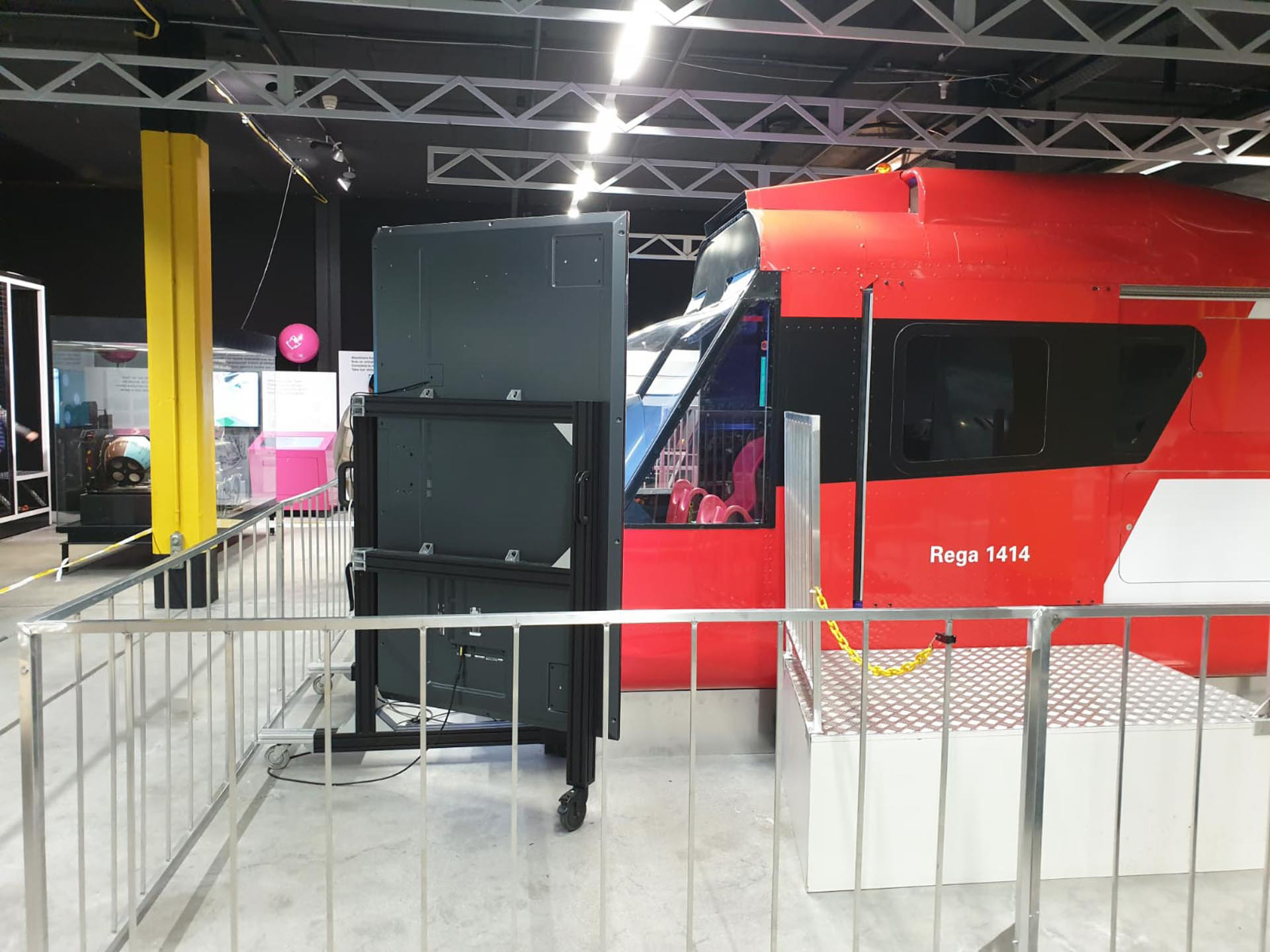 Rotes Helikopter-Cockpit mit Aufschrift Rega 1414 in einer Ausstellung, umgeben von Metallgeländern.