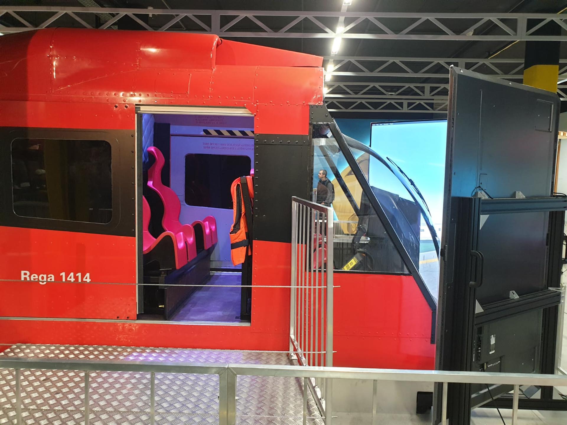 Roter Helikopter-Simulator mit pinkfarbenen Sitzen und Bildschirmen in einer Ausstellung.