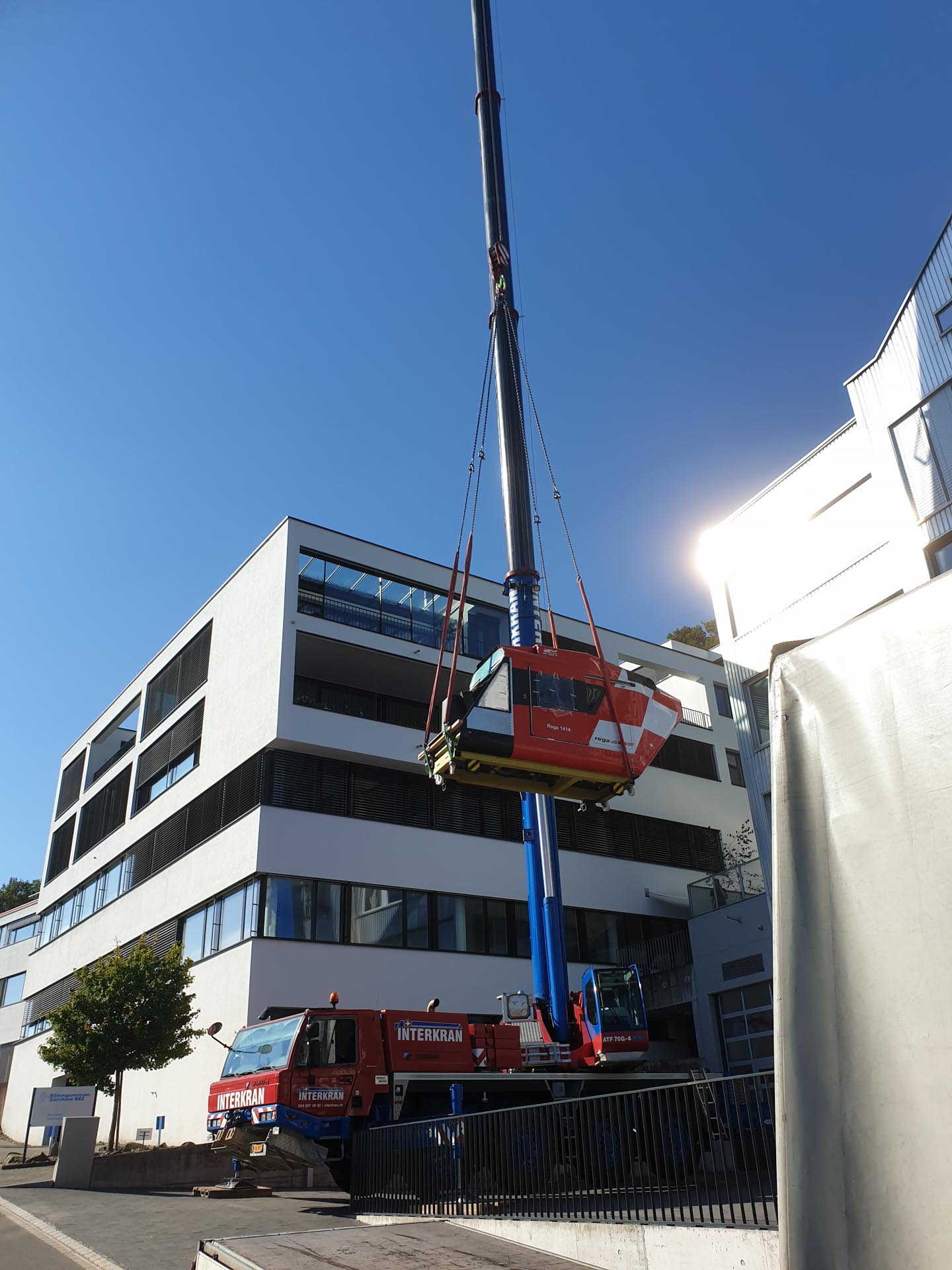 Ein roter Kran hebt die Kabine eines Rettungshubschraubers vor einem modernen Gebäude.