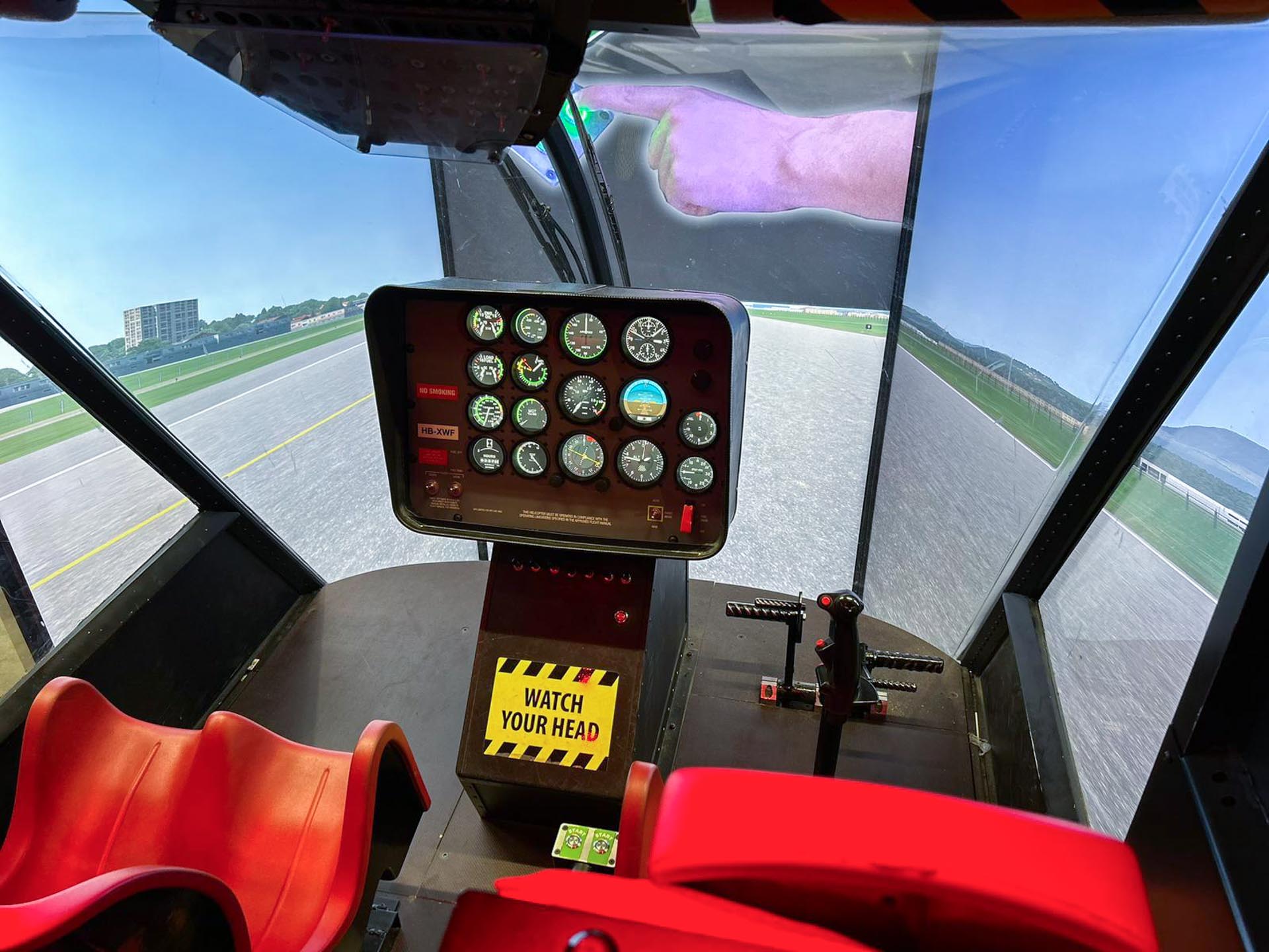 Helikopter-Cockpit mit Kontrollanzeigen, Steuerhebel, rotem Sitz und Warnschild „Watch Your Head“.