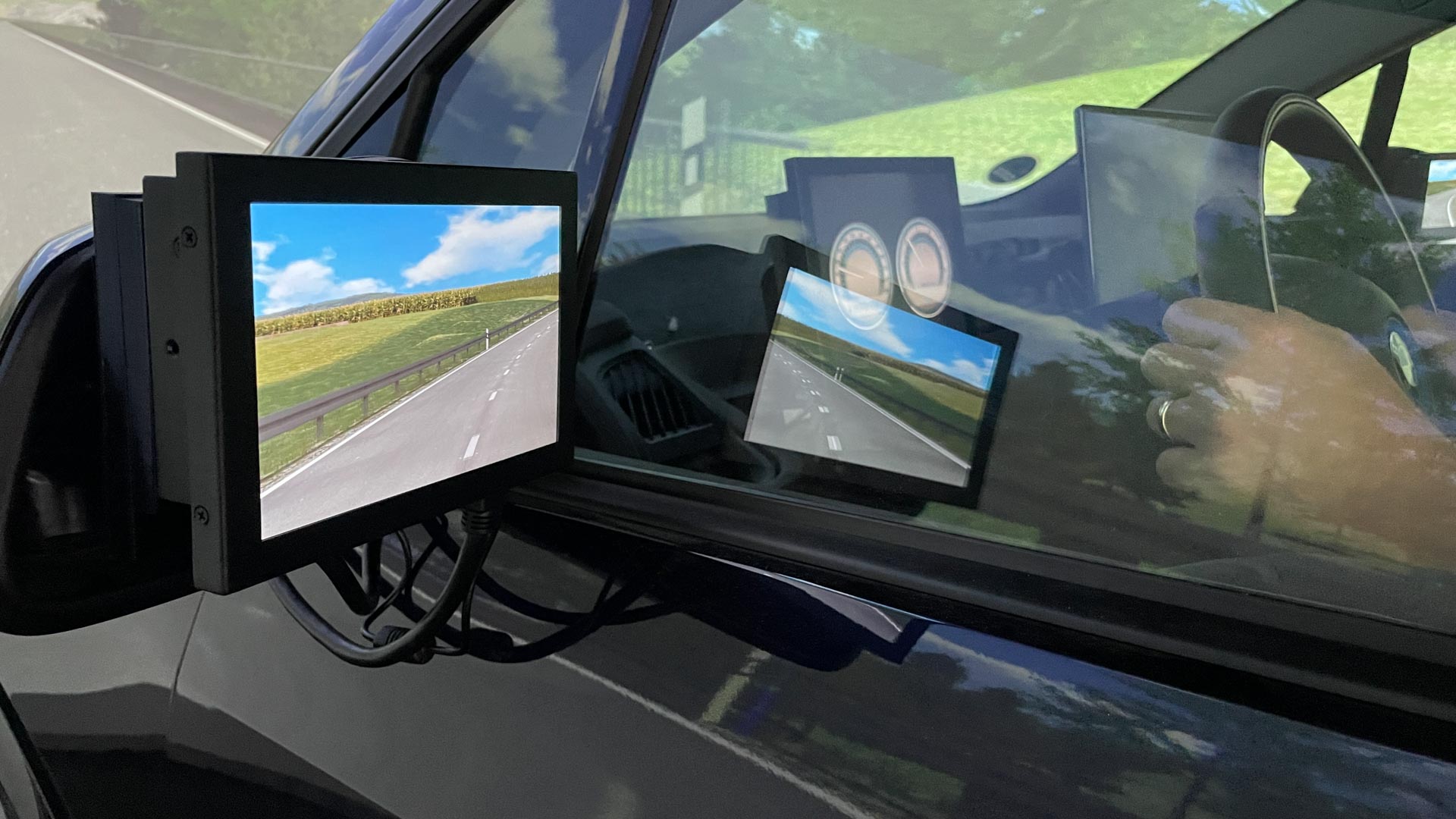 L'écran, à la place du rétroviseur d'une voiture, montre une route de campagne avec un ciel bleu.