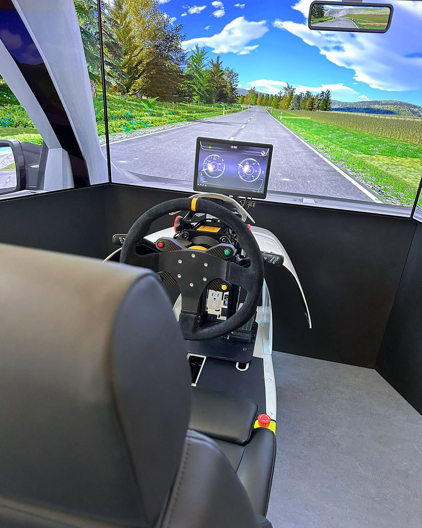 Le simulateur de conduite avec volant, siège et écran montre une route de campagne avec des arbres et des montagnes.