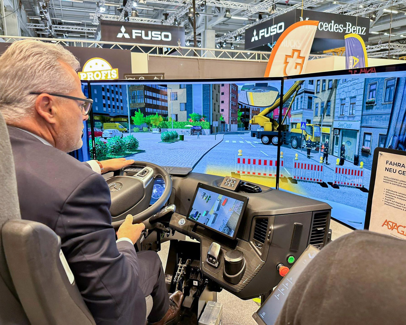 Mann testet LKW-Fahrsimulator mit großem Bildschirm, der urbane Straßenszene zeigt.