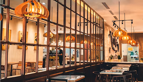 Interior of a cozy café with warm lighting, wooden chairs, tables, and large window panes reflecting pendant lamps.