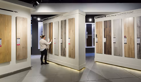 Person standing in a showroom examining different laminate flooring samples displayed on angled white panels.