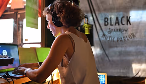 Two people using a laptop at Black Sparrow Music Parlor, one wearing headphones.