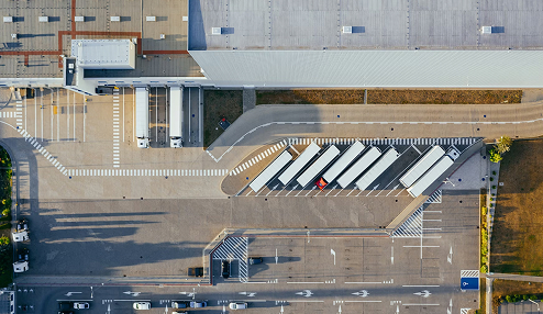 Aerial view of a logistics facility with several trucks parked in loading bays and vehicles moving on the access road.