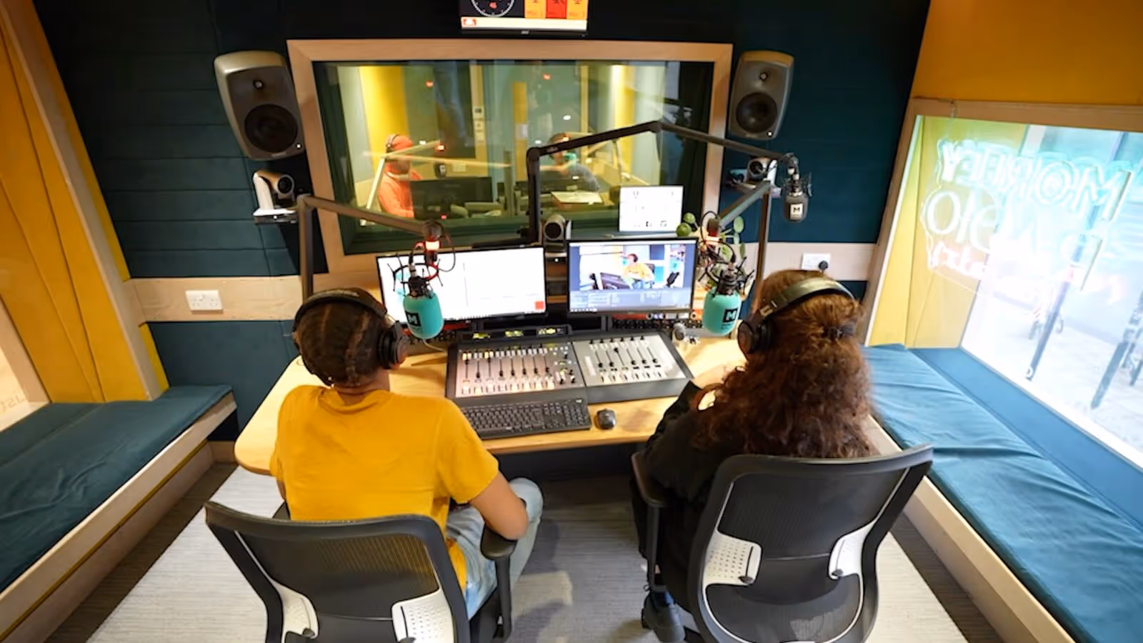 Two radio hosts wearing headphones sitting at a broadcast mixer with microphones in a studio.