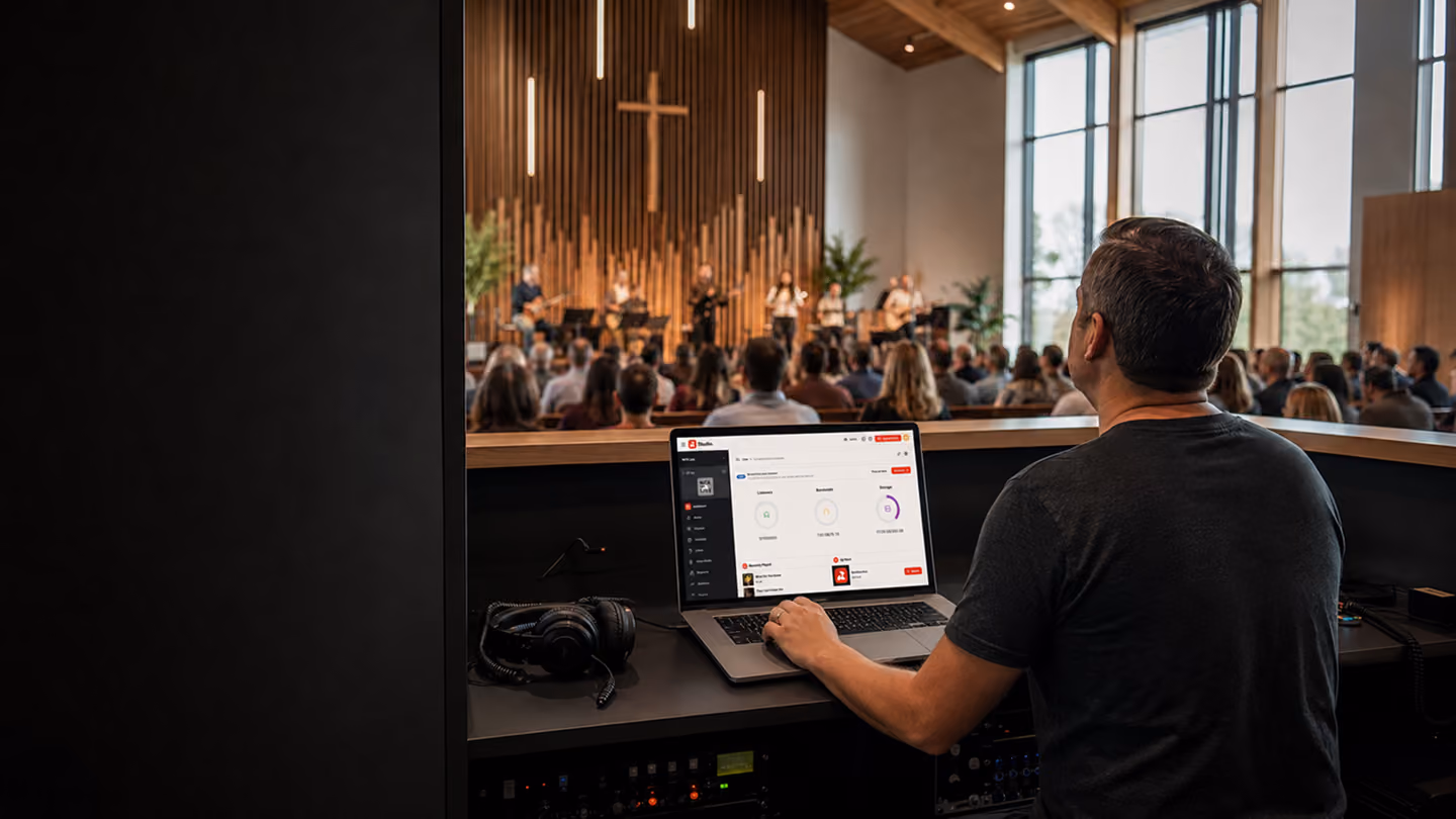 Man operating a laptop in a sound booth during a church service with a worship band and congregation.