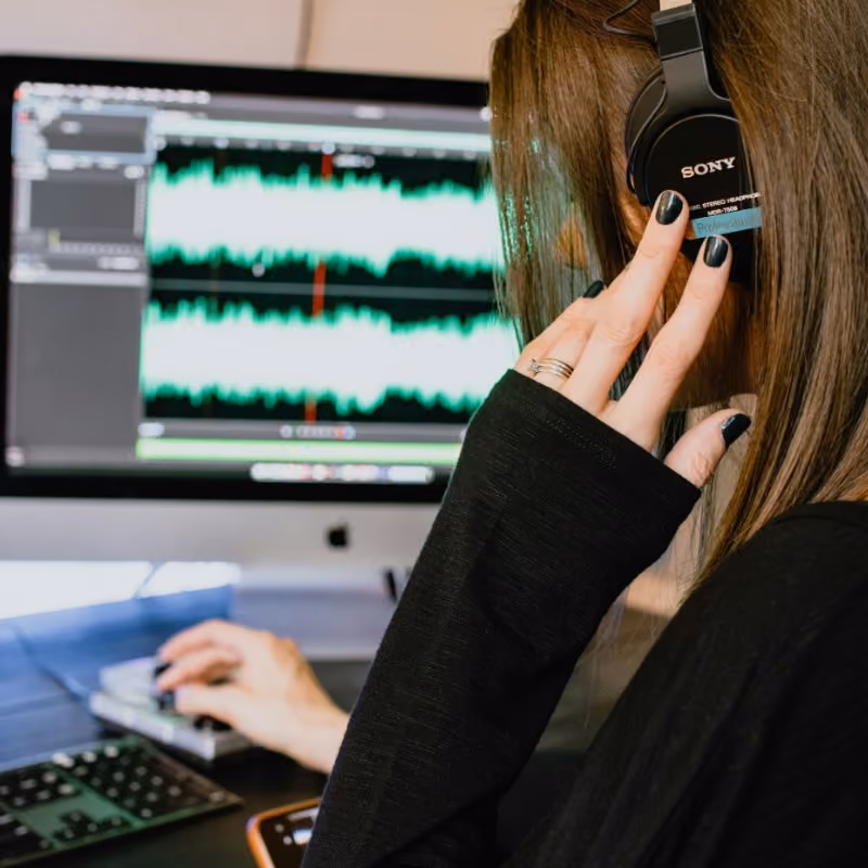 Person wearing Sony headphones editing audio waveforms on a computer screen.