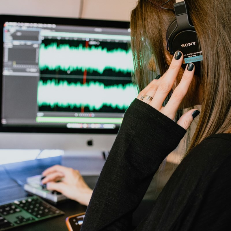 Person wearing Sony headphones editing audio waveforms on a computer screen.
