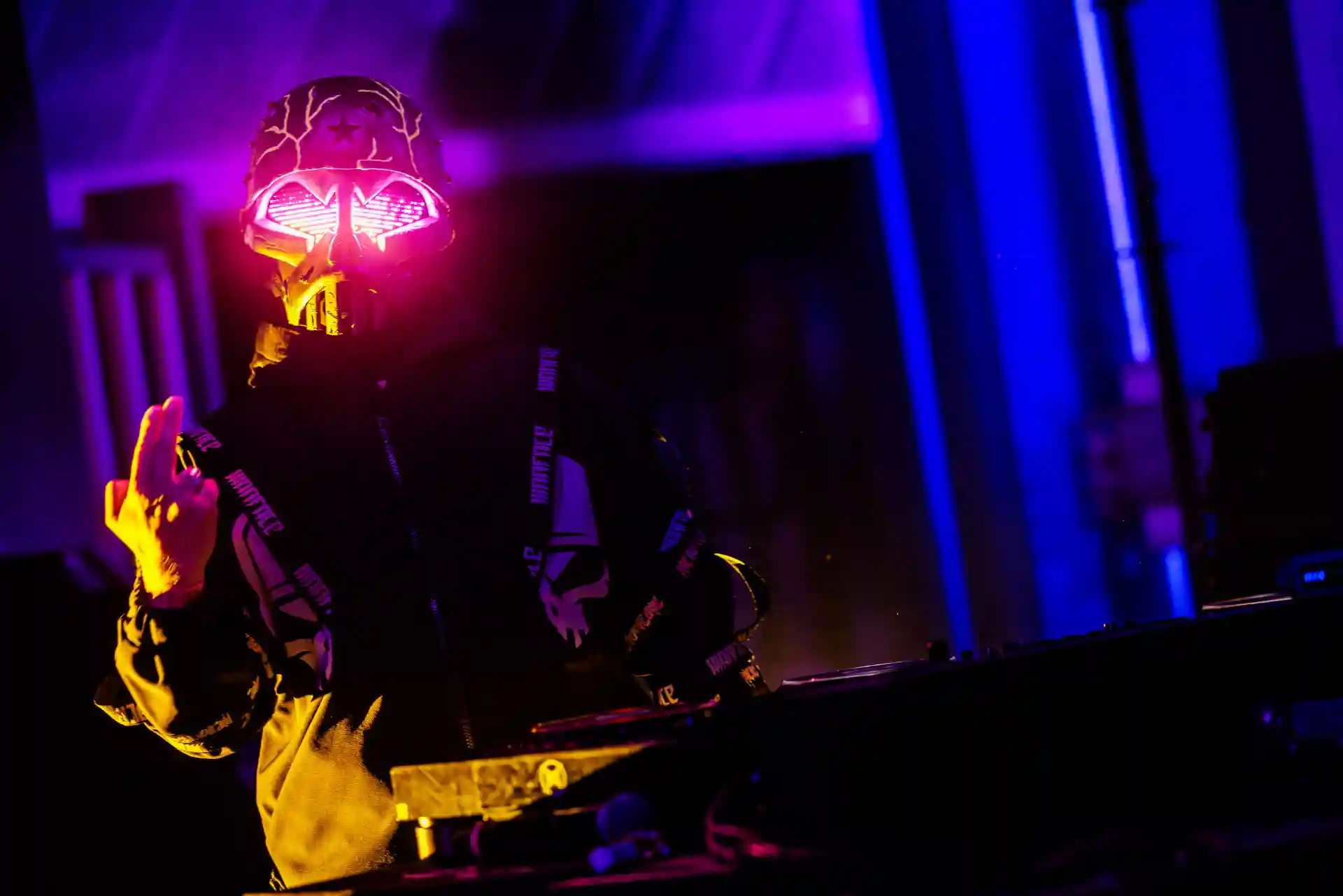 Decibel Outdoor DJ with glowing mask performing under purple and blue lights