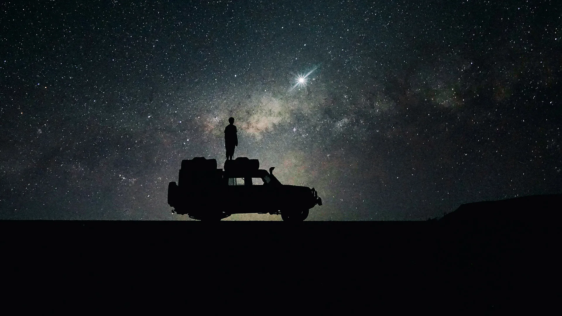 Person on top of a 4x4 vehicle observing the night sky