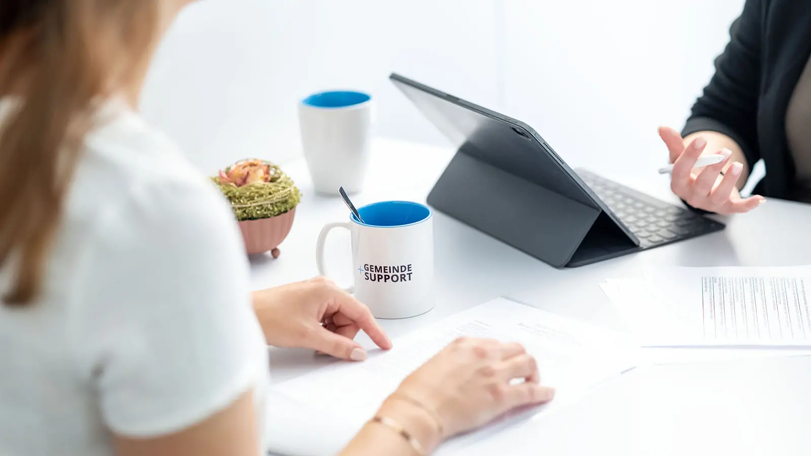 Mitarbeiterinnen der Gemeindeverwaltung besprechen Dokumente und Aufgaben am Tisch mit Tablet und Unterlagen