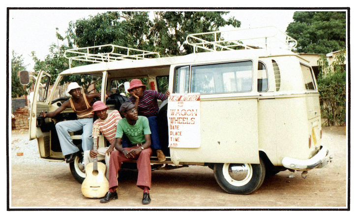 Oliver Mtukudzi and the band the Wagon Wheels sitting with their legs hanging outside a van.