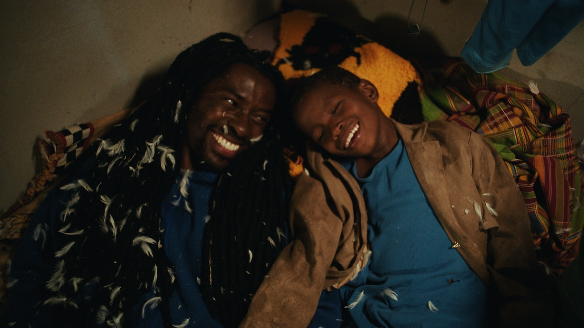 A man and a young boy, sprinkled in feathers, lie on a mattress.