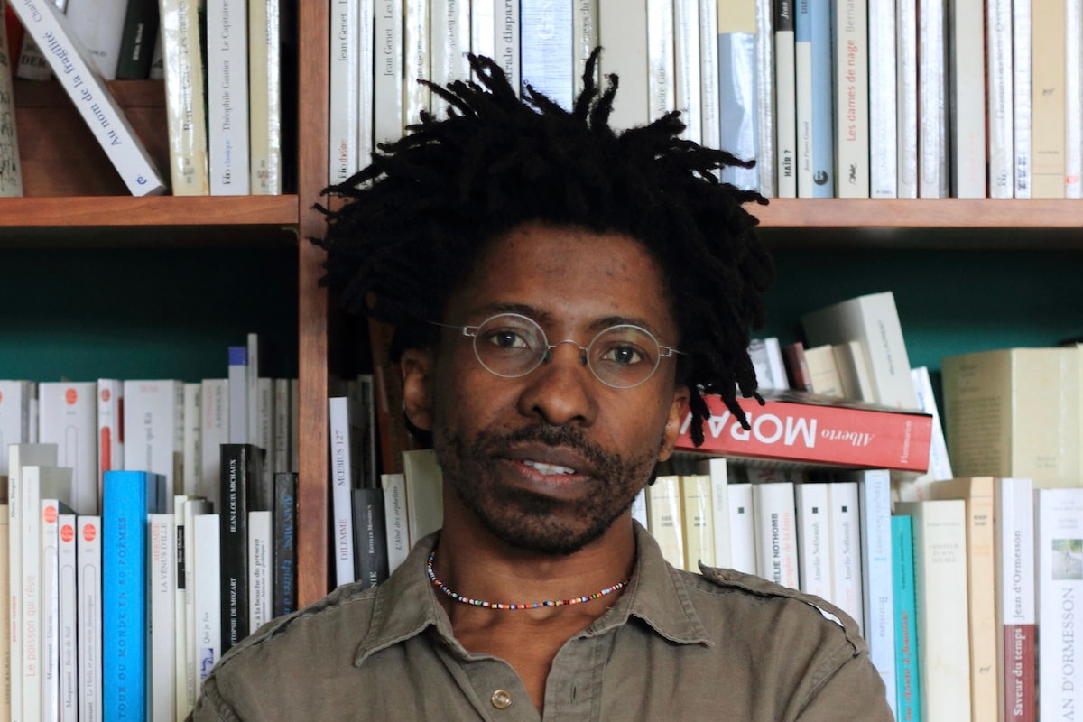 A portrait of author Brian Chikwava in front of a bookshelf.