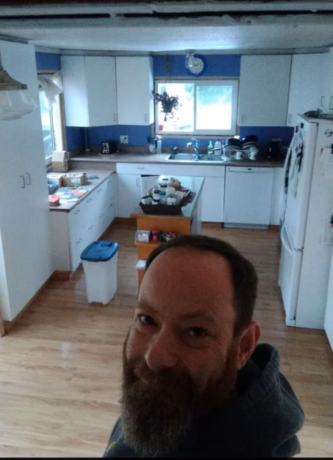 Chris Warren in front of the completed work:

✔️Cabinet re-facing with sage colored shaker doors and drawer fronts. Painted former white gable ends to match
✔️Acacia Chevron Butcher Block Countertop, oiled with food grade finish 
✔️ Tongue and groove knotty pine v-groove 1x6 ceiling throughout kitchen, dining, and hallway 
✔️Sterling Oak 7mm  Click Lock Waterproof Luxury Vinyl Plank Flooring throughout kitchen, dining, hallway and mud room.  
✔️Tiled backsplash 
✔️ Natural wood window finishes with insulation and vapour barrier ensured first 
✔️ Douglas fir stained baseboards #
✔️ Remodeled buffet also with butcher block featuring custom vinyl record dividers.  Deleted ceiling valance 
✔️Fresh paint in kitchen &  dining rooms
✔️Restored kitchen island with matching countertop, addition of shaker doors, fir base and sage paint.
✔️ Updated light fixtures and a couple of switch and plug replacements
✔️ Stainless steel appliances install, (hood fan, dishwasher and fridge 
