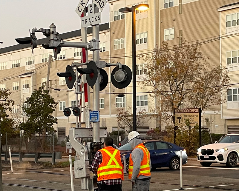Two workers in PPE inspecting railroad crossing equipment near at Norwood Depot station.