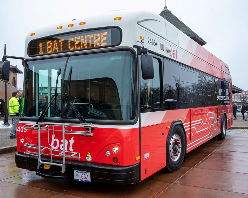 A red and white battery electric bus from Brocton Area Transit with destination sign reading '1 BAT CENTRE' parked at a bus stop.