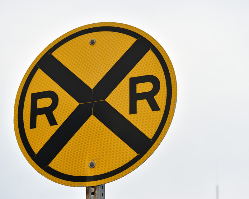 Yellow circular railroad crossing road sign with black X and the letters R on each side.