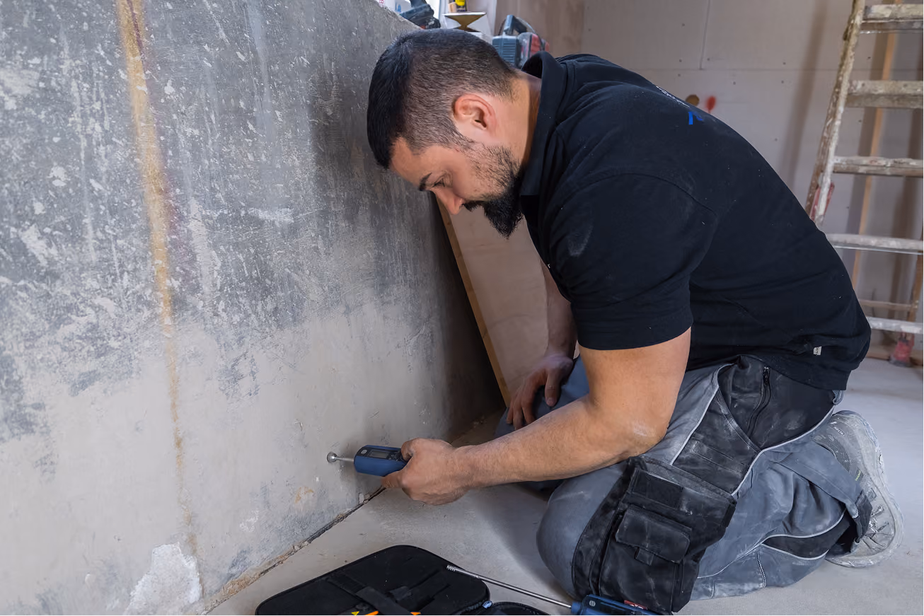 Messgerät Hydromette UNI 2 zeigt 25,8 mit zwei Sensoren an einem Holzboden und weißer Wand.
