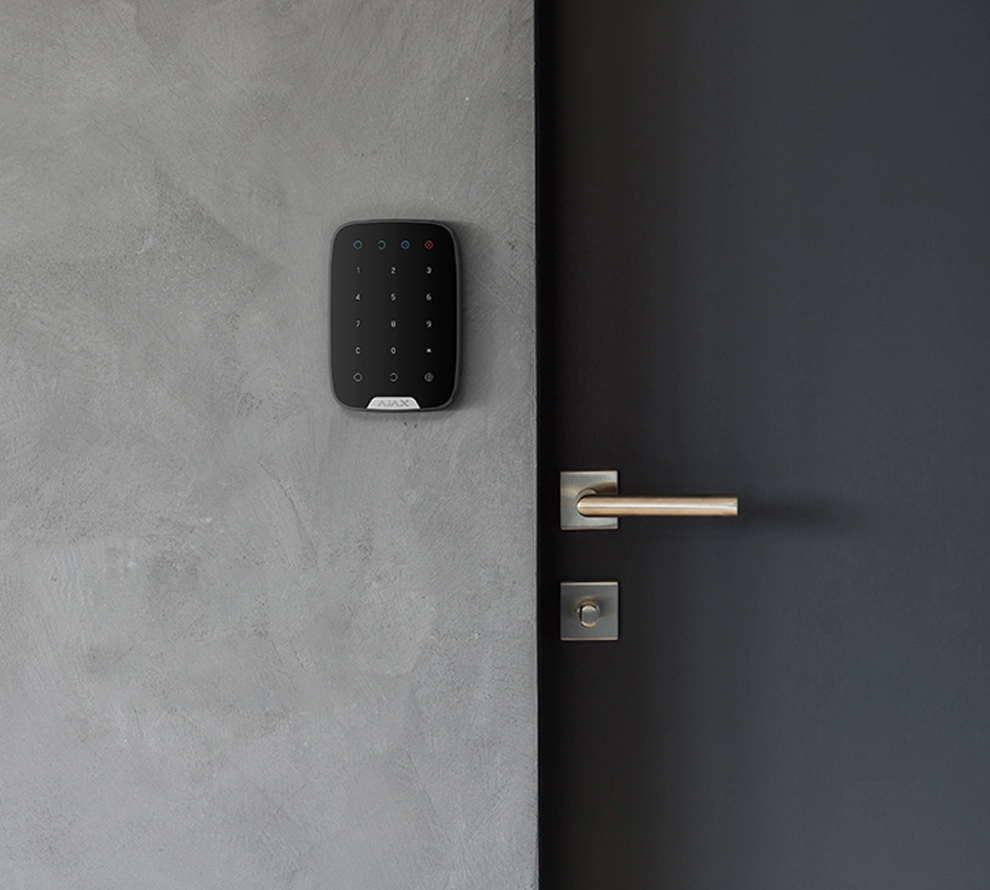 Black numeric keypad security device mounted on gray wall next to black door with silver handle.
