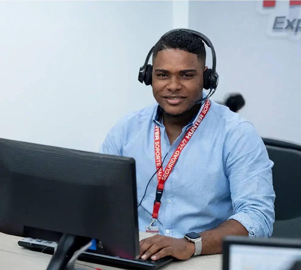 Smiling customer service representative wearing headset and blue shirt, working at a desk with a computer.