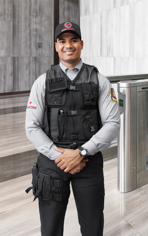 Smiling security officer in uniform standing beside a white police motorcycle holding a helmet in a parking area.