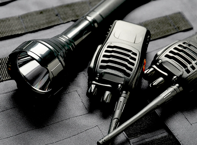 Two black walkie-talkies and a metal flashlight placed on a dark fabric surface.
