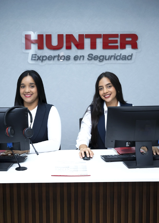 Two women smiling at desks with computers below a sign that reads HUNTER Expertos en Seguridad.