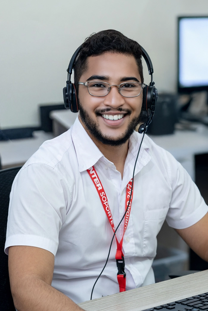 Smiling man with glasses wearing a headset and white shirt at a desk, working in a support center.