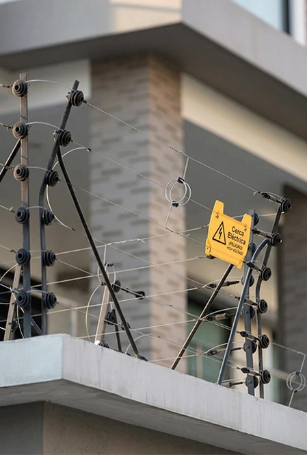 Electric fence on top of a building wall with a yellow warning sign that reads 'Cerca Eléctrica Peligro No Tocar'.