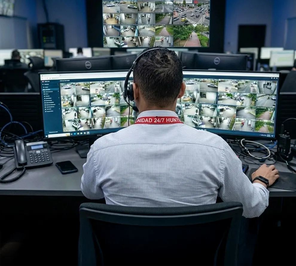 Security officer monitoring surveillance footage on multiple screens in a control room.
