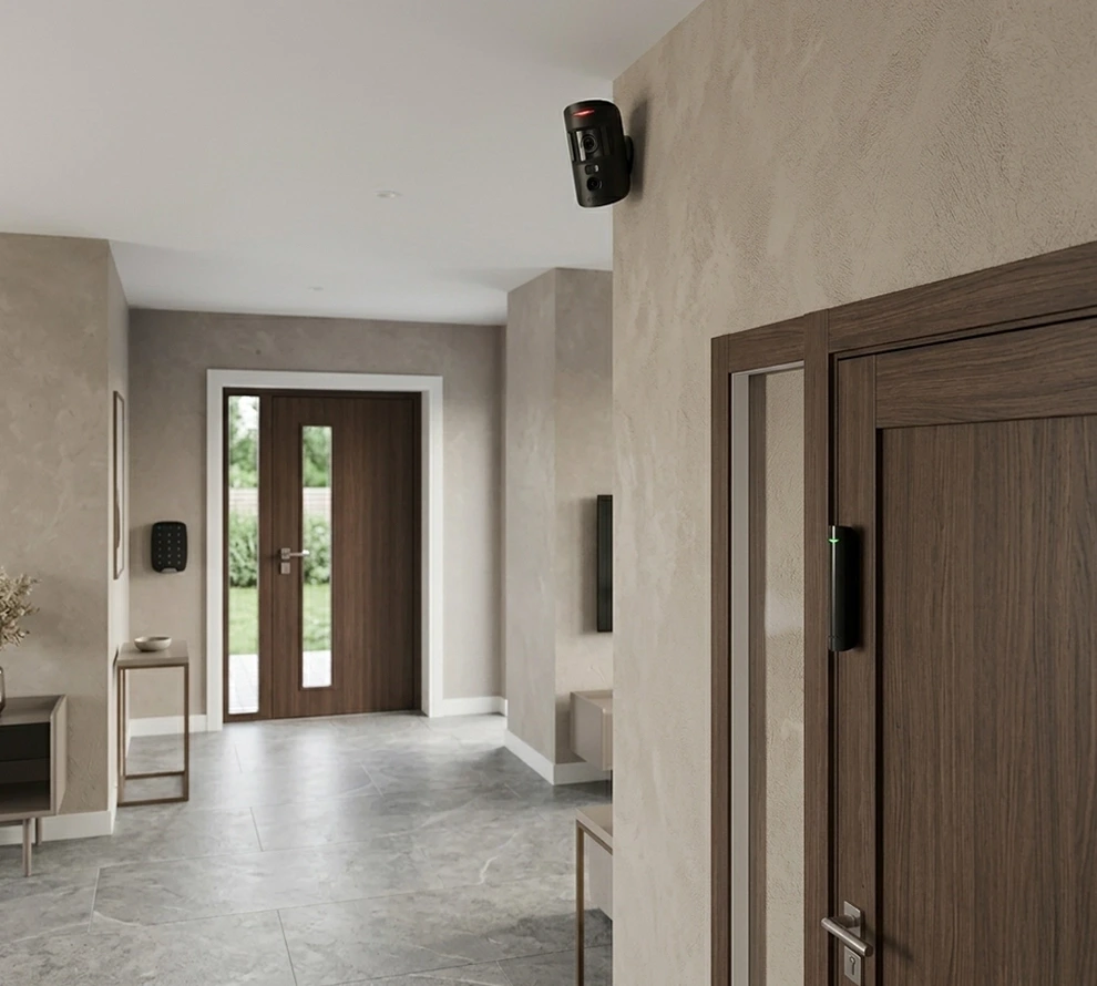 Modern indoor hallway with wooden doors, security camera mounted on the wall, and access control keypad near the entrance.