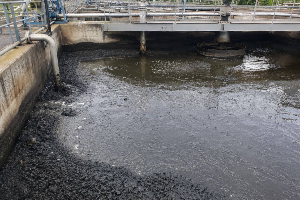 Industrial wastewater basin showing heavy sludge accumulation along walls and reduced treatment efficiency