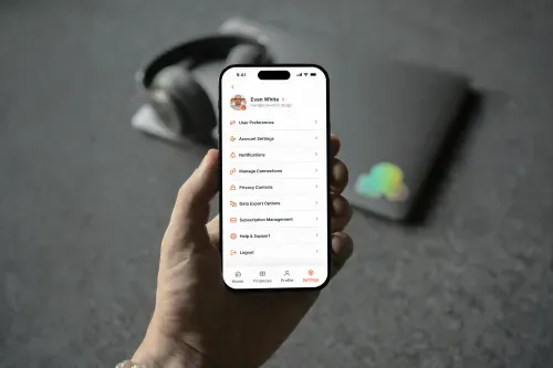 Hand holding smartphone displaying user account settings menu with options like User Preferences, Account Settings, Notifications, and Logout.